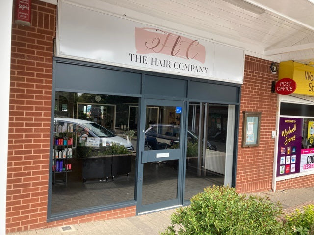 Image of the Storefront of 'The Hair Company' with a brick exterior and Aluminium glass doors. The single door has a letter box.