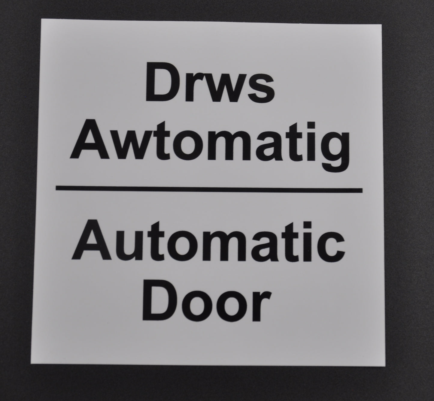 A white self-adhesive automatic door sign with black text, indicating 'Automatic Door' in English and 'Drws Awtomatig' in Welsh. On grey background.