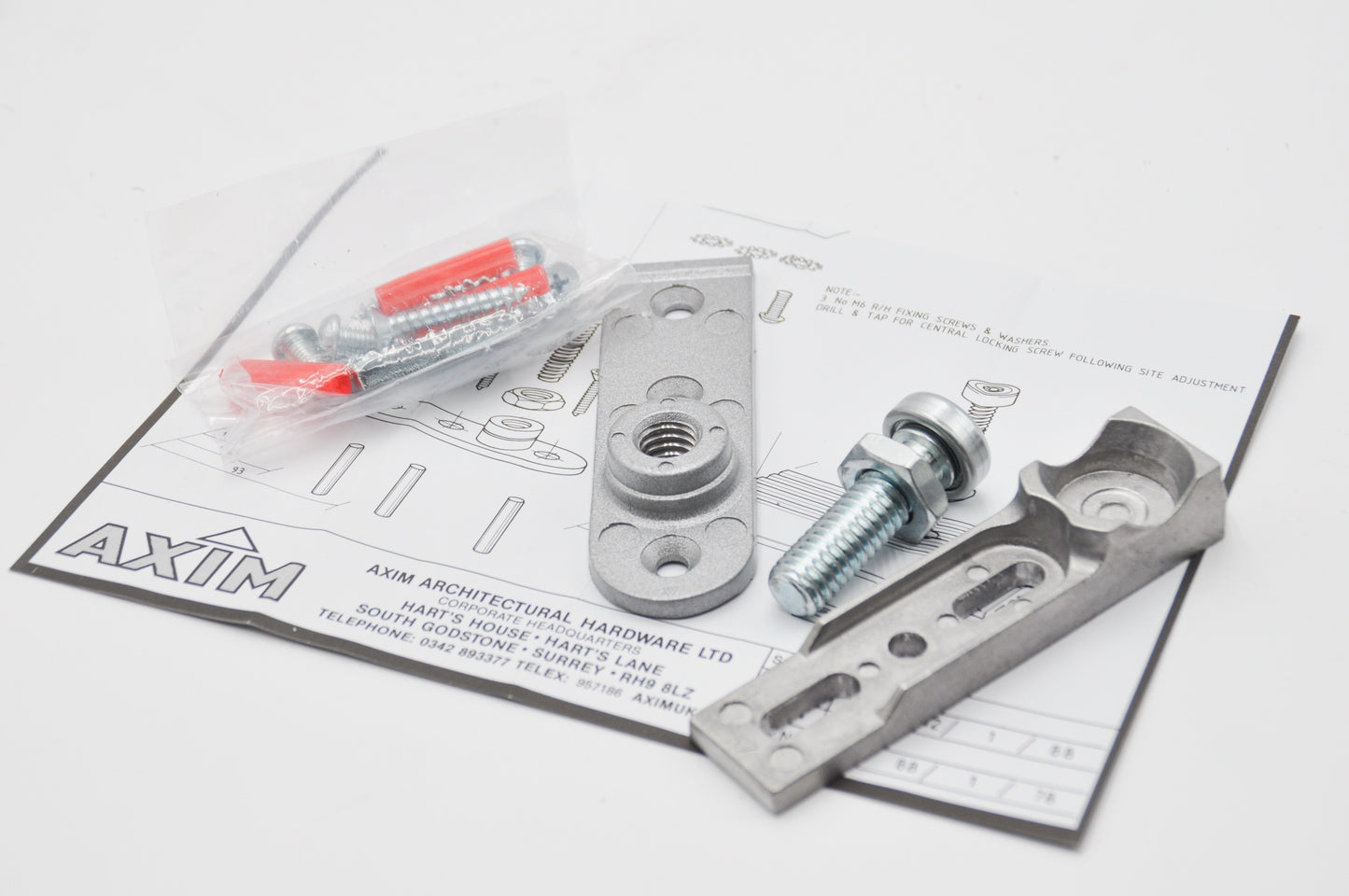 An image showing two components of the Axim TC-8800-02 Aluminium Door Bottom Pivot, including a pivot point and an attachment plate, both made from aluminium, on top on instructions with black text and the Axim logo on with fixings in clear packaging. On a white background.