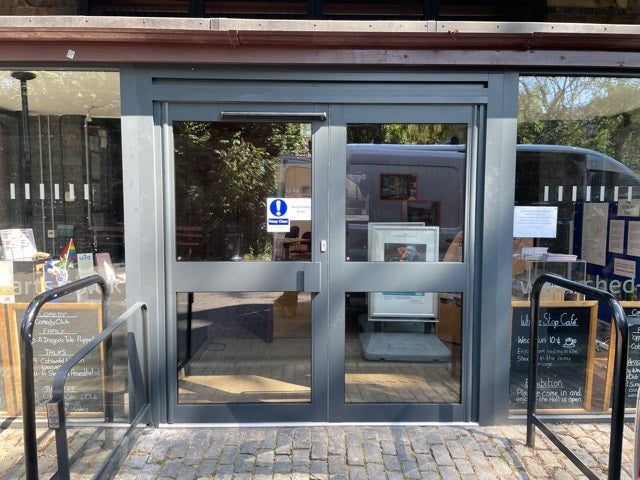 Aluminium and glass door entrance to a building.  Signage indicating Keep clear and Automatic door.  Automatic door safety barriers either side.